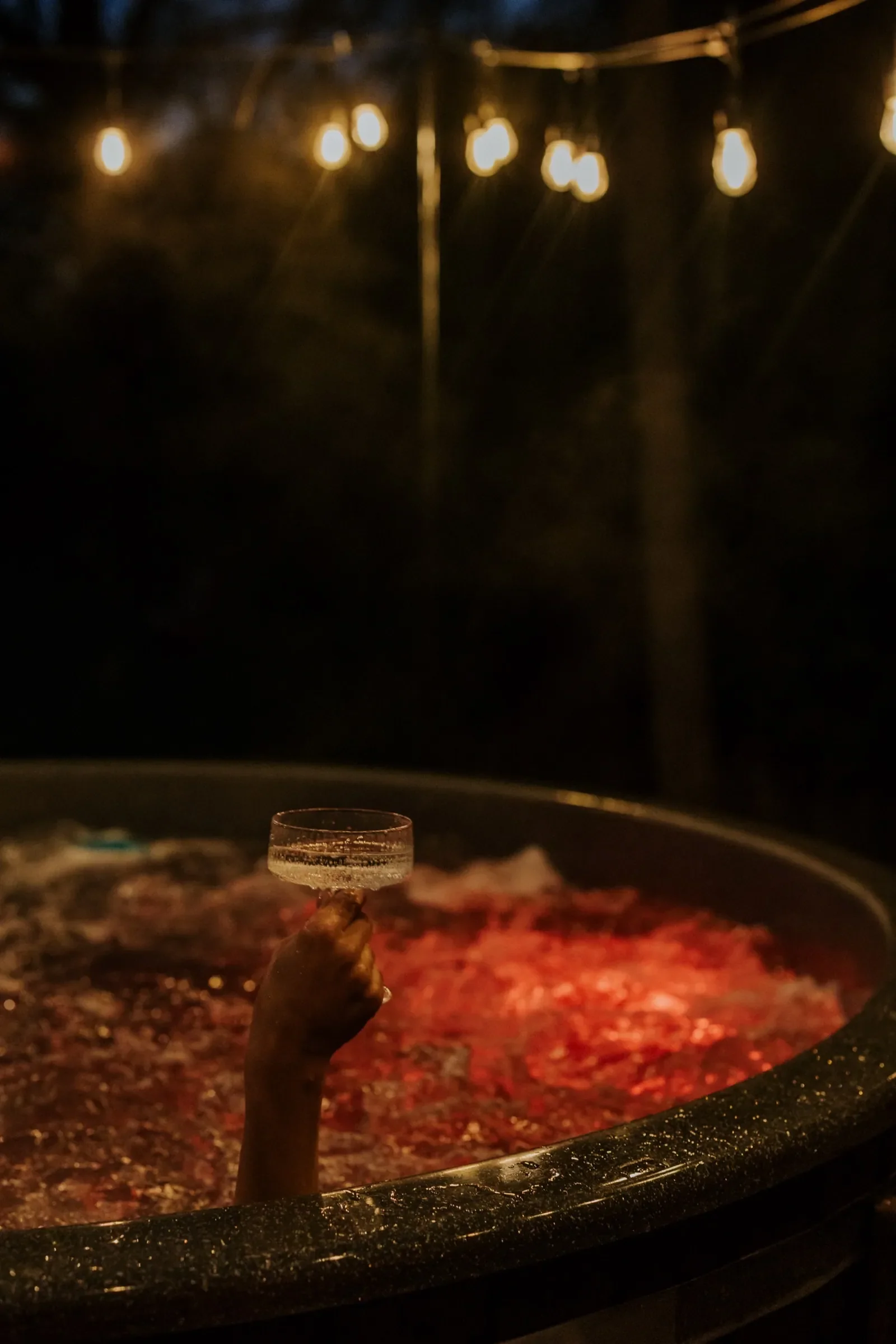 Drink w dłoni nad rozgrzaną balią, czerwone światło po zmroku