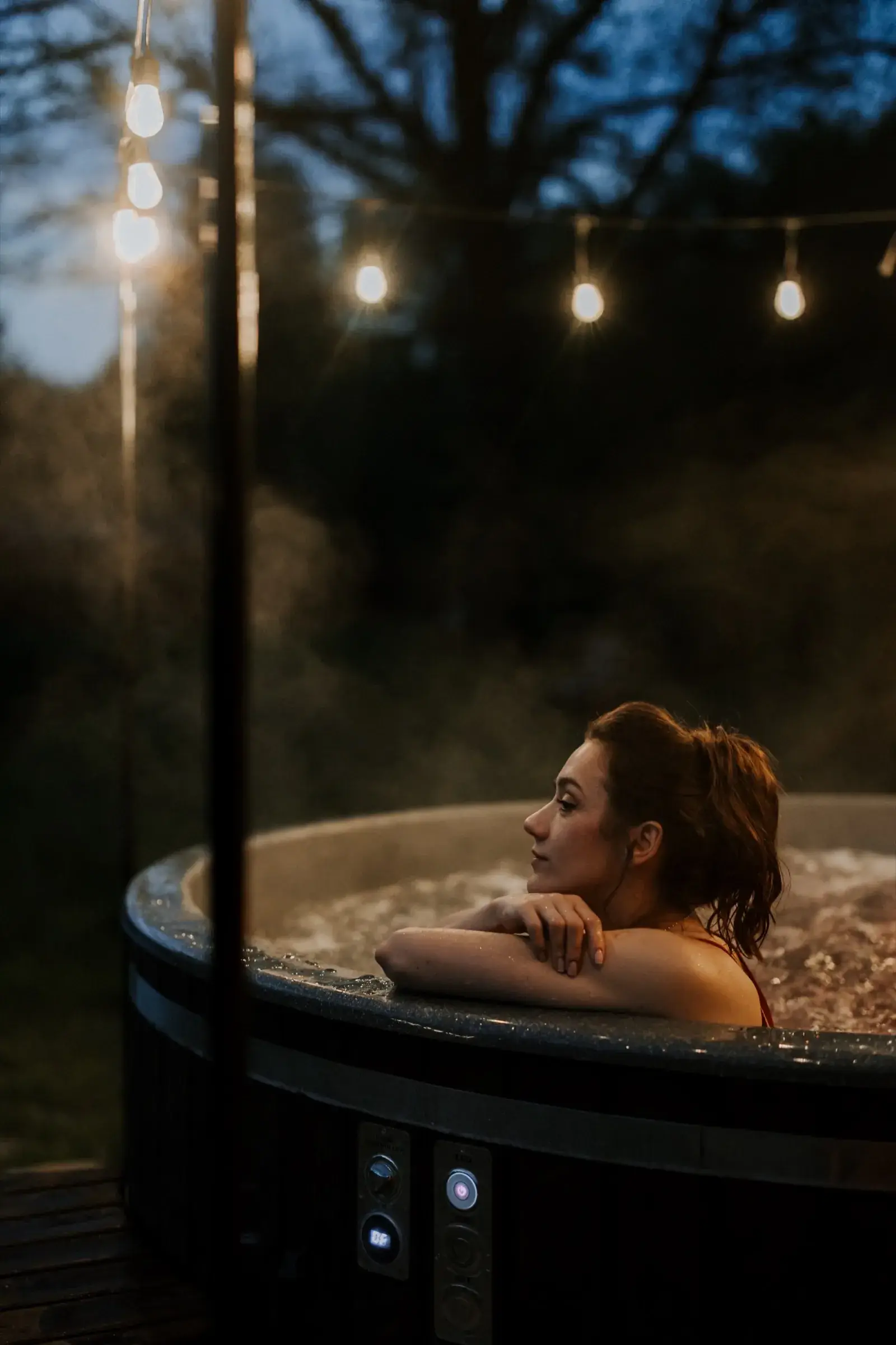 Kobieta w balii z jacuzzi wieczorem, girlandy świetlne nad wodą